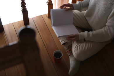 Woman with cup of coffee reading book at home, closeup