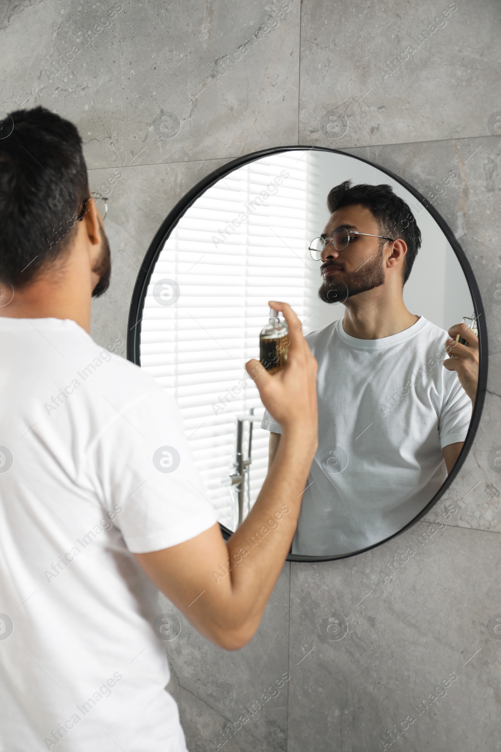 Photo of Man spraying luxury perfume near mirror indoors