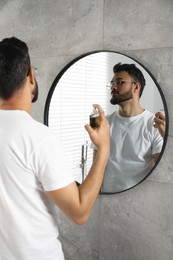 Man spraying luxury perfume near mirror indoors