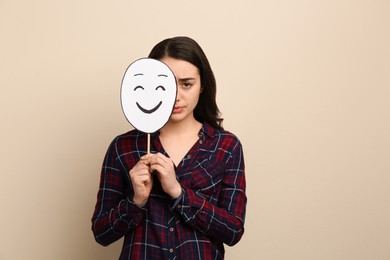 Photo of Sad woman hiding behind happy paper face on beige background