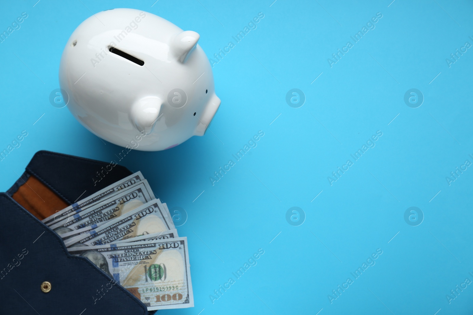 Photo of Piggy bank and wallet with banknotes on light blue background, flat lay. Space for text