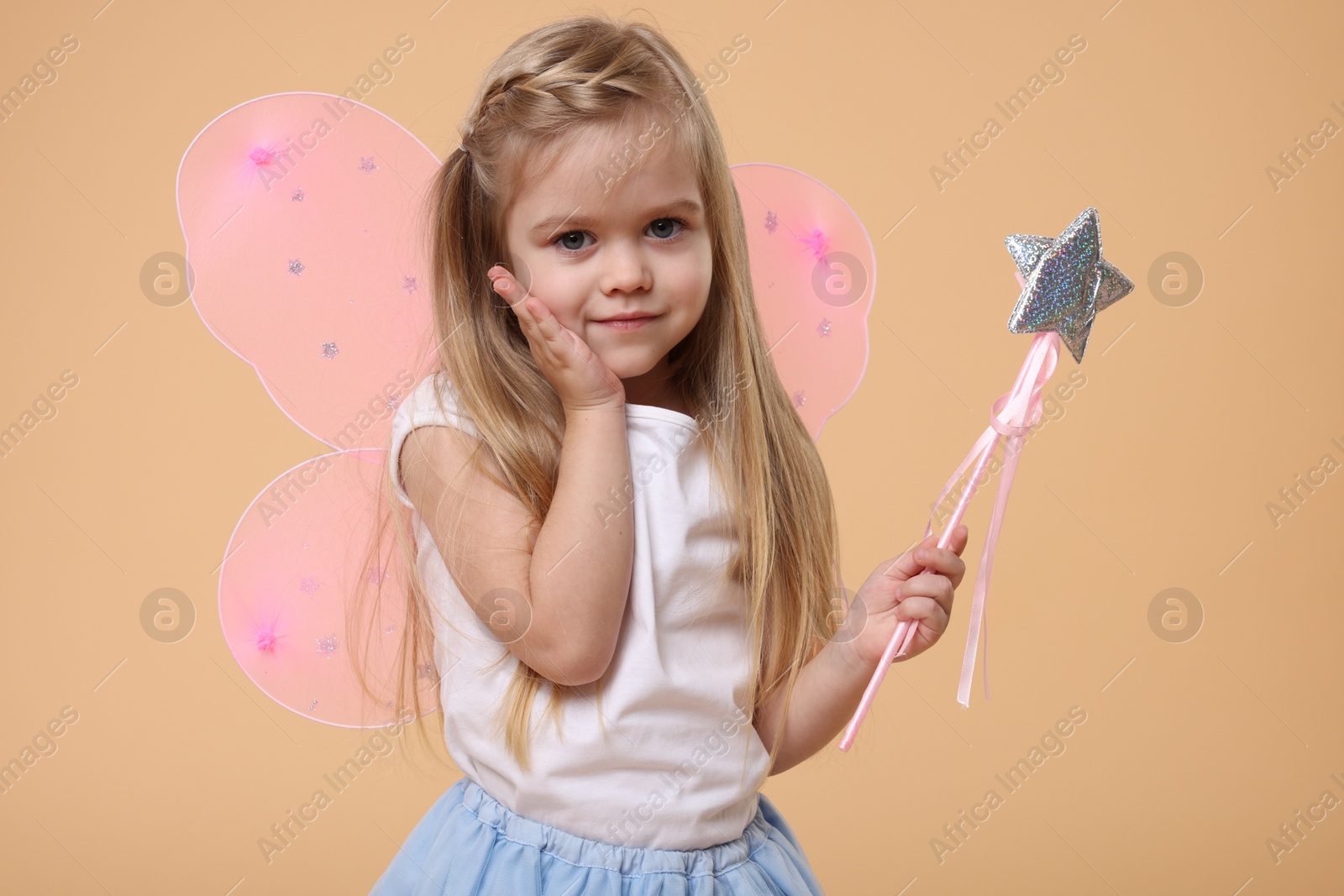 Photo of Cute little girl in fairy costume with pink wings and magic wand on beige background