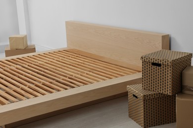 Photo of New wooden bed frame and moving boxes indoors