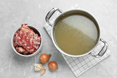Photo of Pot with delicious bone broth and ingredients on light grey table, flat lay