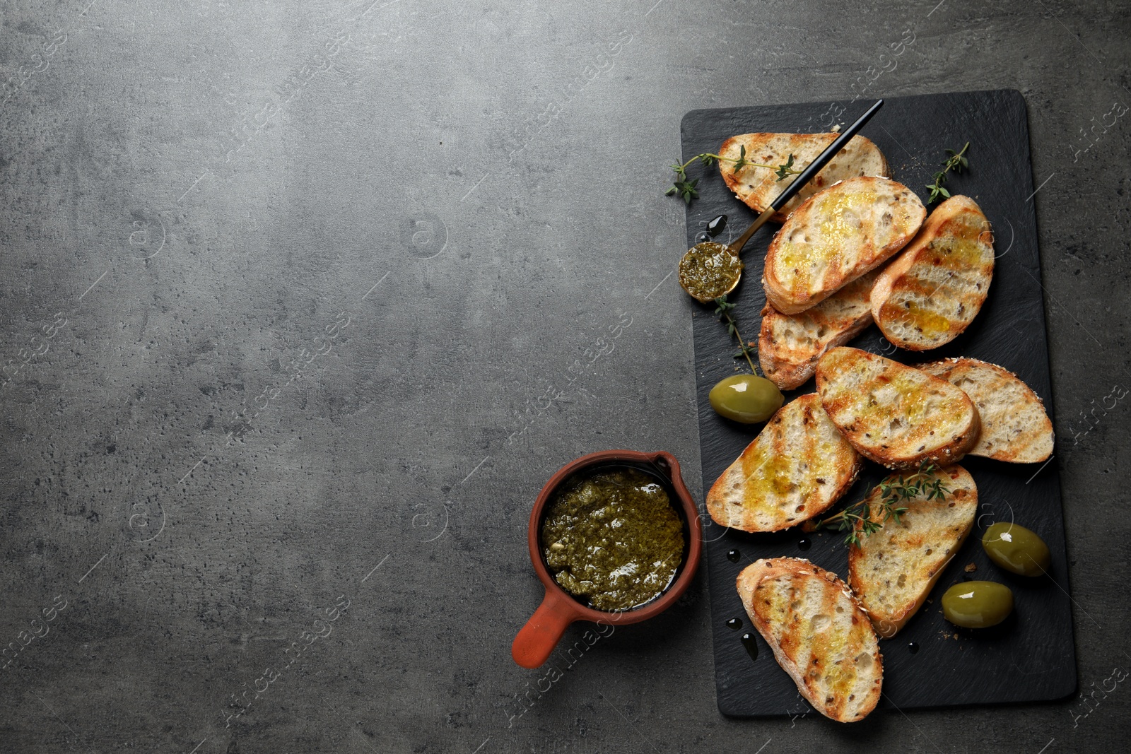 Photo of Tasty bruschettas with oil, thyme and olives on grey table, flat lay. Space for text