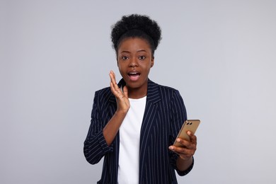 Photo of Emotional young woman with smartphone on light grey background