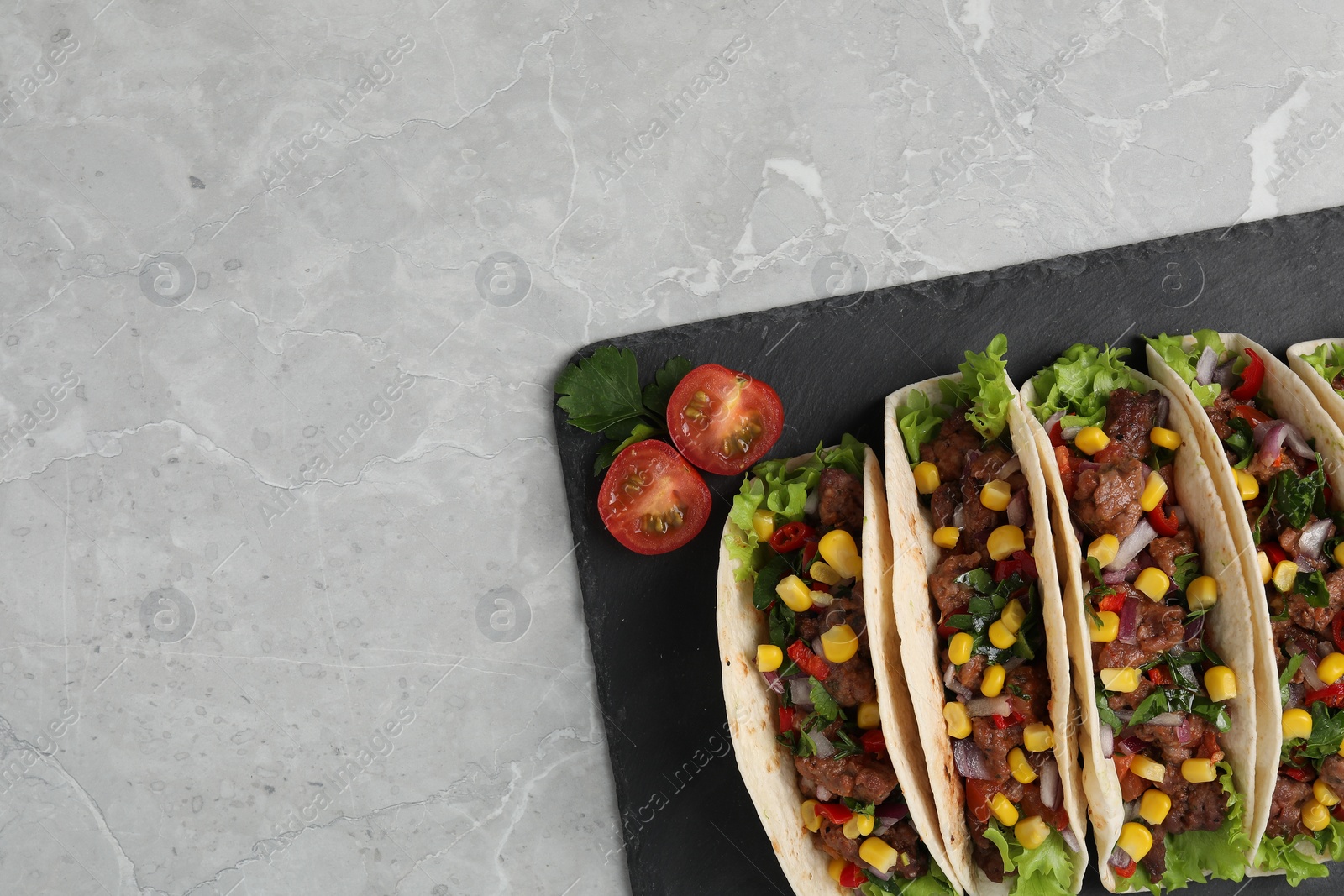 Photo of Delicious tacos with meat and vegetables on light gray marble table, top view. Space for text