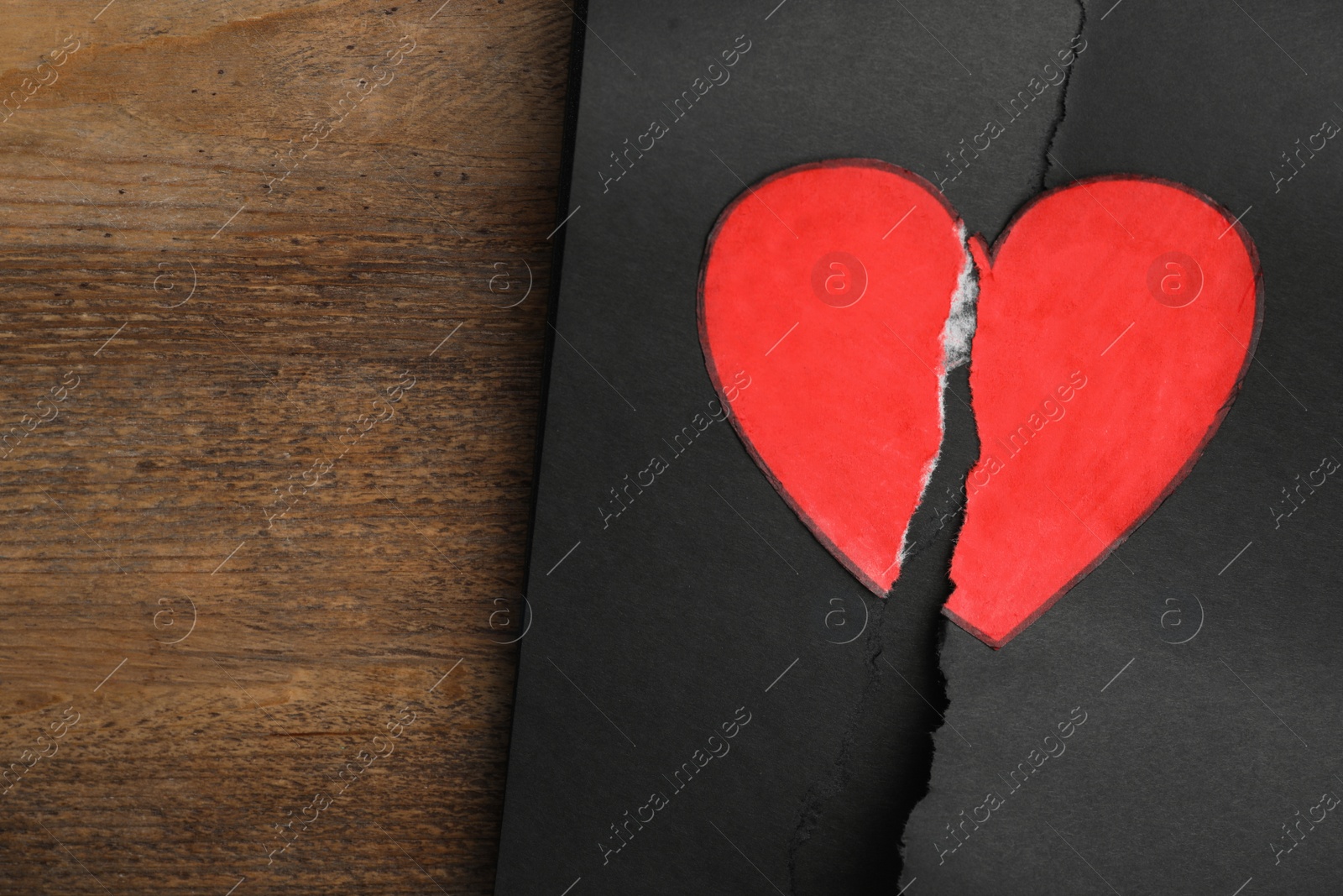 Photo of Torn black sheet with heart sticker on wooden background, top view. Relationship problems concept