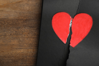 Photo of Torn black sheet with heart sticker on wooden background, top view. Relationship problems concept