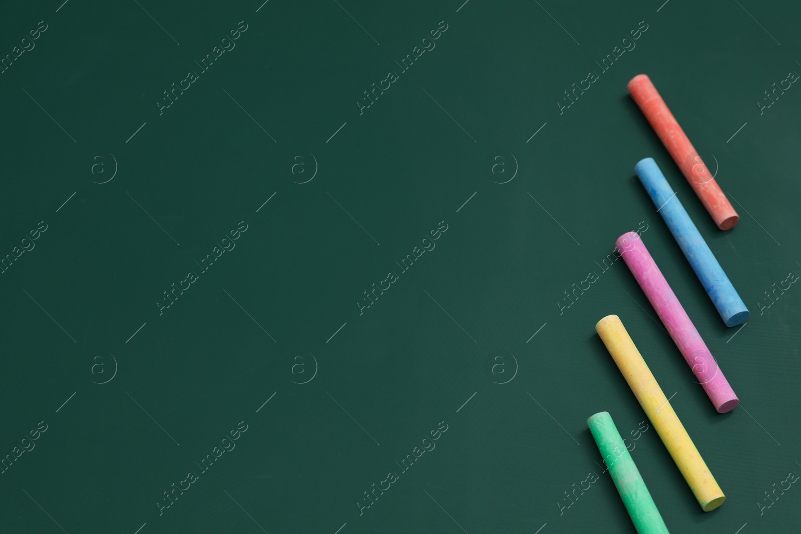 Photo of Colorful chalks on green board, above view. Space for text