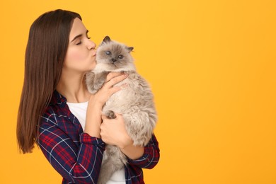 Photo of Woman kissing her cute cat on orange background, space for text