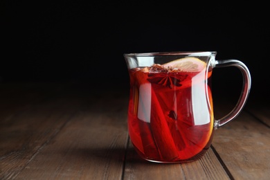 Photo of Cup with red mulled wine on wooden table against dark background. Space for text