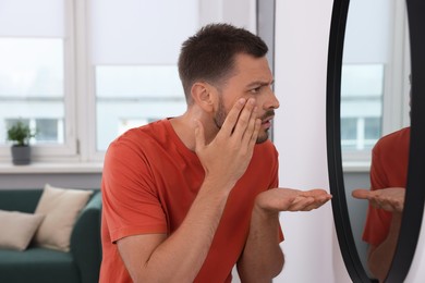Photo of Sleep deprived man looking at himself in mirror indoors