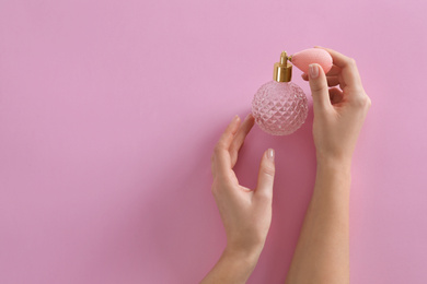Woman with bottle of perfume on pink background, top view. Space for text