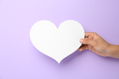 Photo of Woman holding blank paper heart on violet background, closeup. Space for text