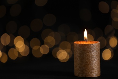 Photo of Burning gold candle against blurred lights in darkness. Space for text