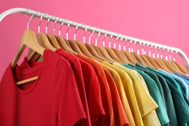 Photo of Rack with bright clothes on pink background. Rainbow colors