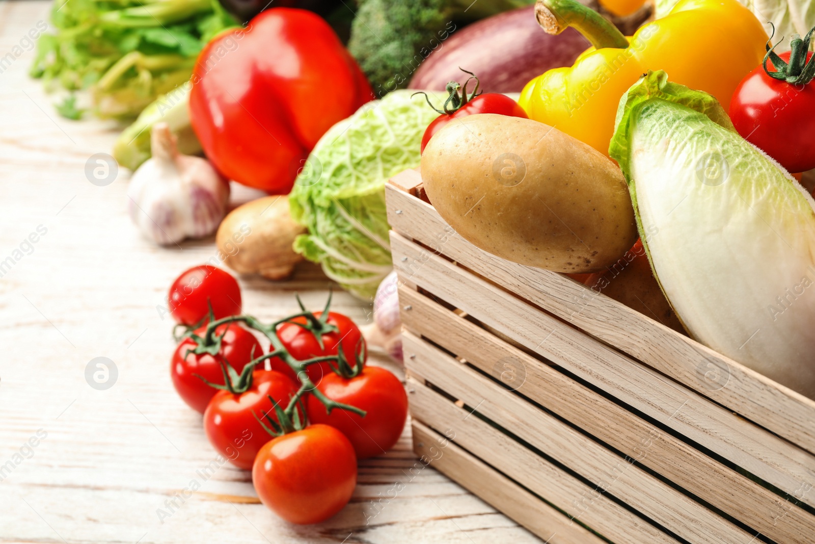 Photo of Fresh vegetables and wooden crate on white table, closeup