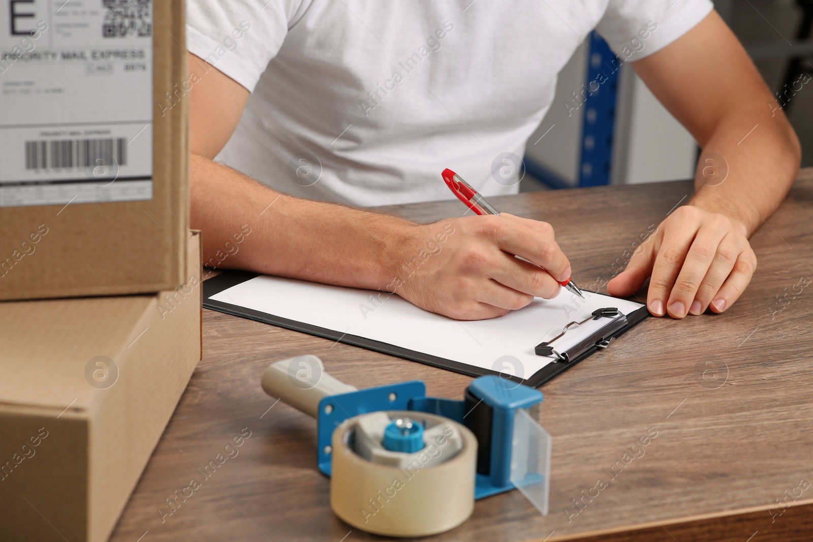 Photo of Post office worker with clipboard and parcels at counter indoors, closeup