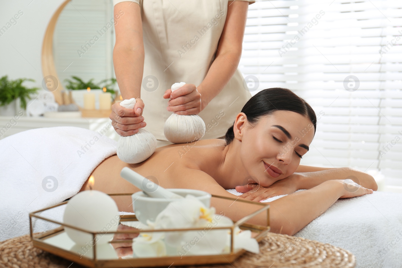 Photo of Young woman receiving herbal bag massage in spa salon