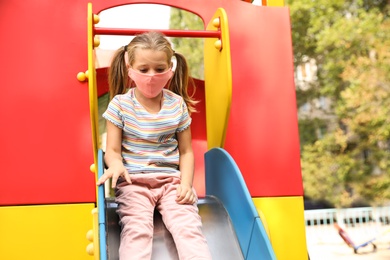 Little girl with medical face mask on playground during covid-19 quarantine