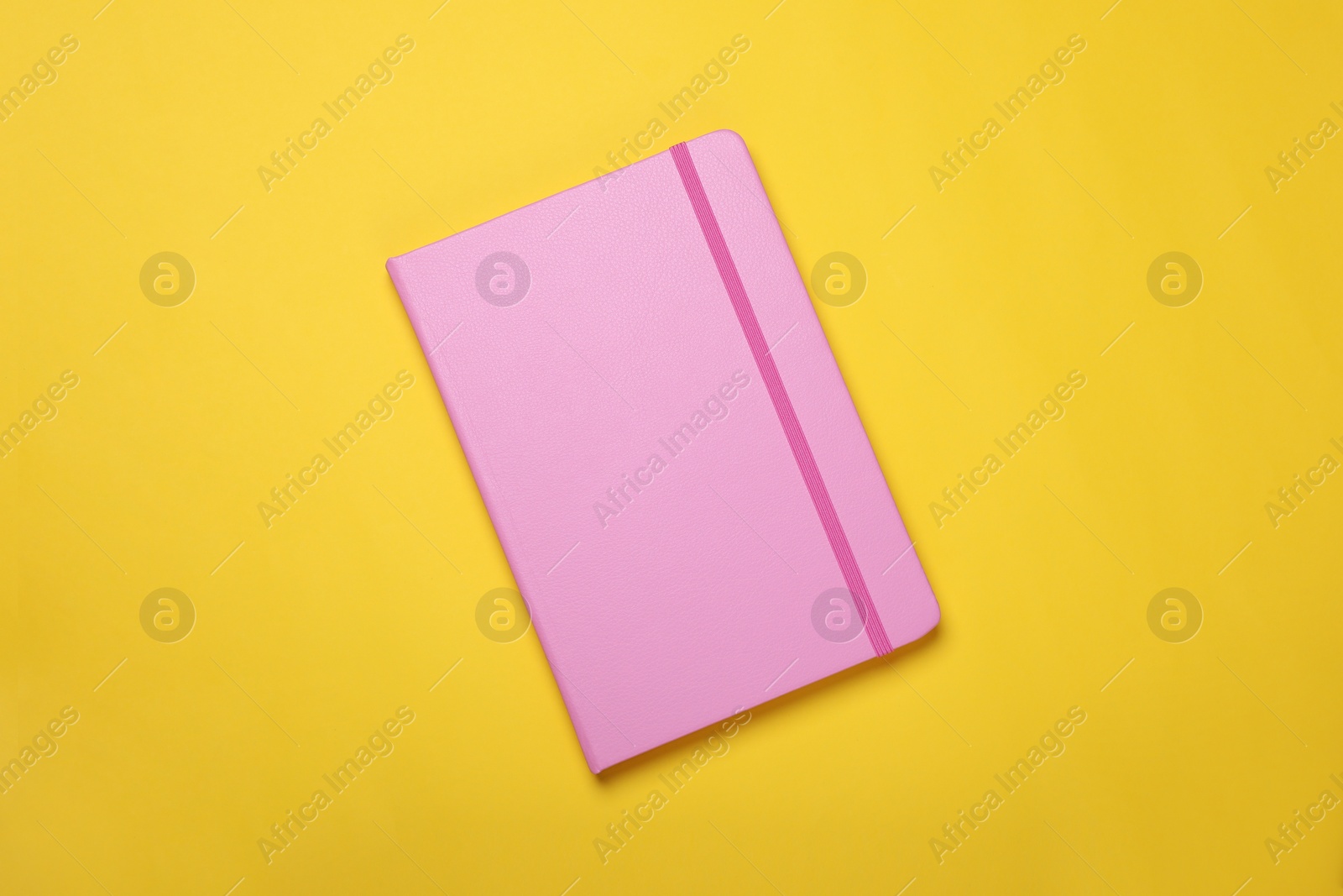 Photo of Closed pink notebook on yellow background, top view