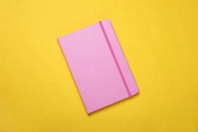 Photo of Closed pink notebook on yellow background, top view
