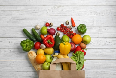 Photo of Paper bag with different groceries on white wooden table, flat lay