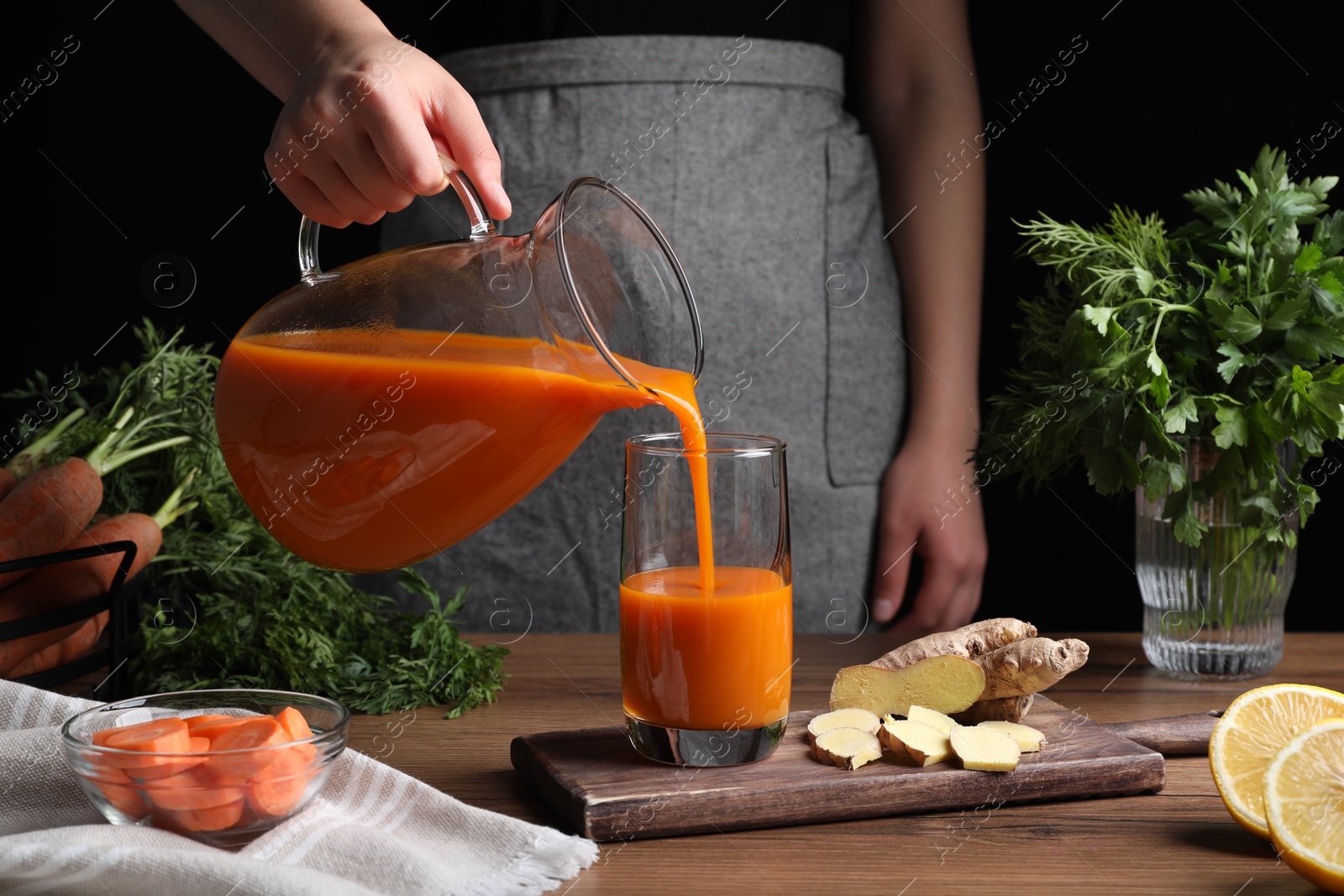 Photo of Woman pouring carrot juice from jug into glass at wooden table, closeup