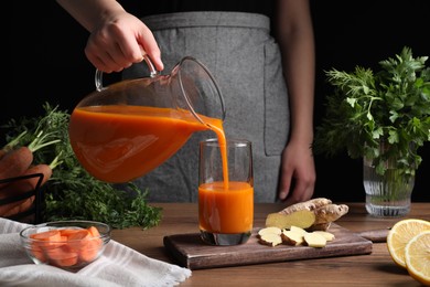 Photo of Woman pouring carrot juice from jug into glass at wooden table, closeup