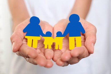Image of Young woman holding paper family figure in colors of Ukrainian flag, closeup of hands