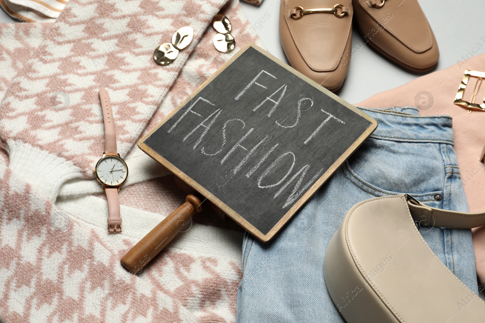 Photo of Small chalkboard with phrase FAST FASHION, stylish clothes and accessories on light background