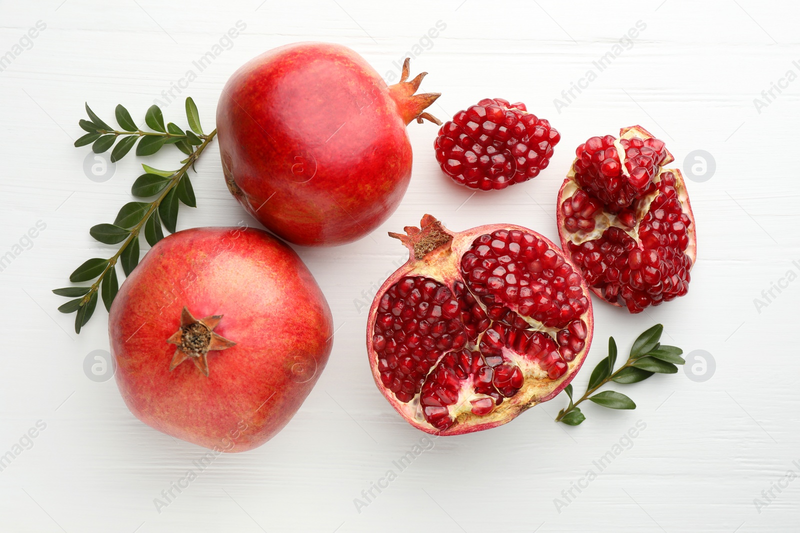 Photo of Pieces of fresh pomegranate and branches on white wooden table, flat lay