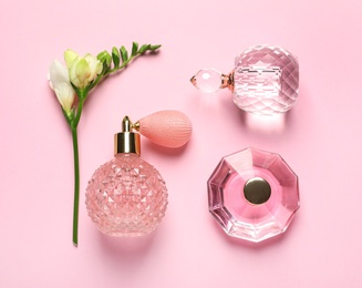 Photo of Flat lay composition with perfume bottles and flowers on light pink background