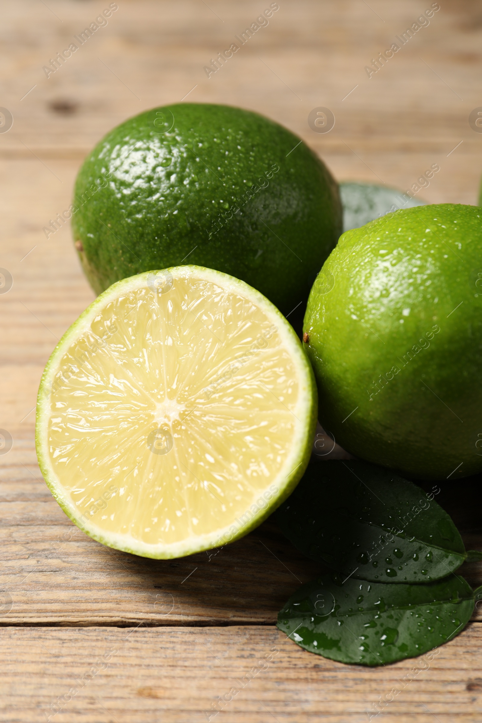 Photo of Fresh limes and green leaves with water drops on wooden table, closeup