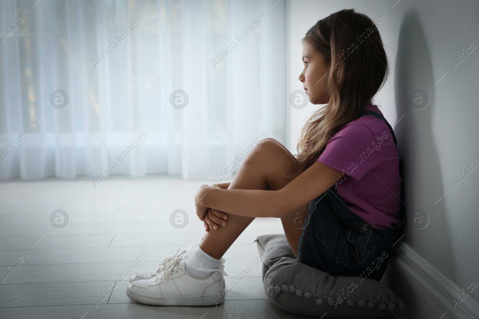 Photo of Sad little girl near white wall indoors, space for text. Domestic violence concept