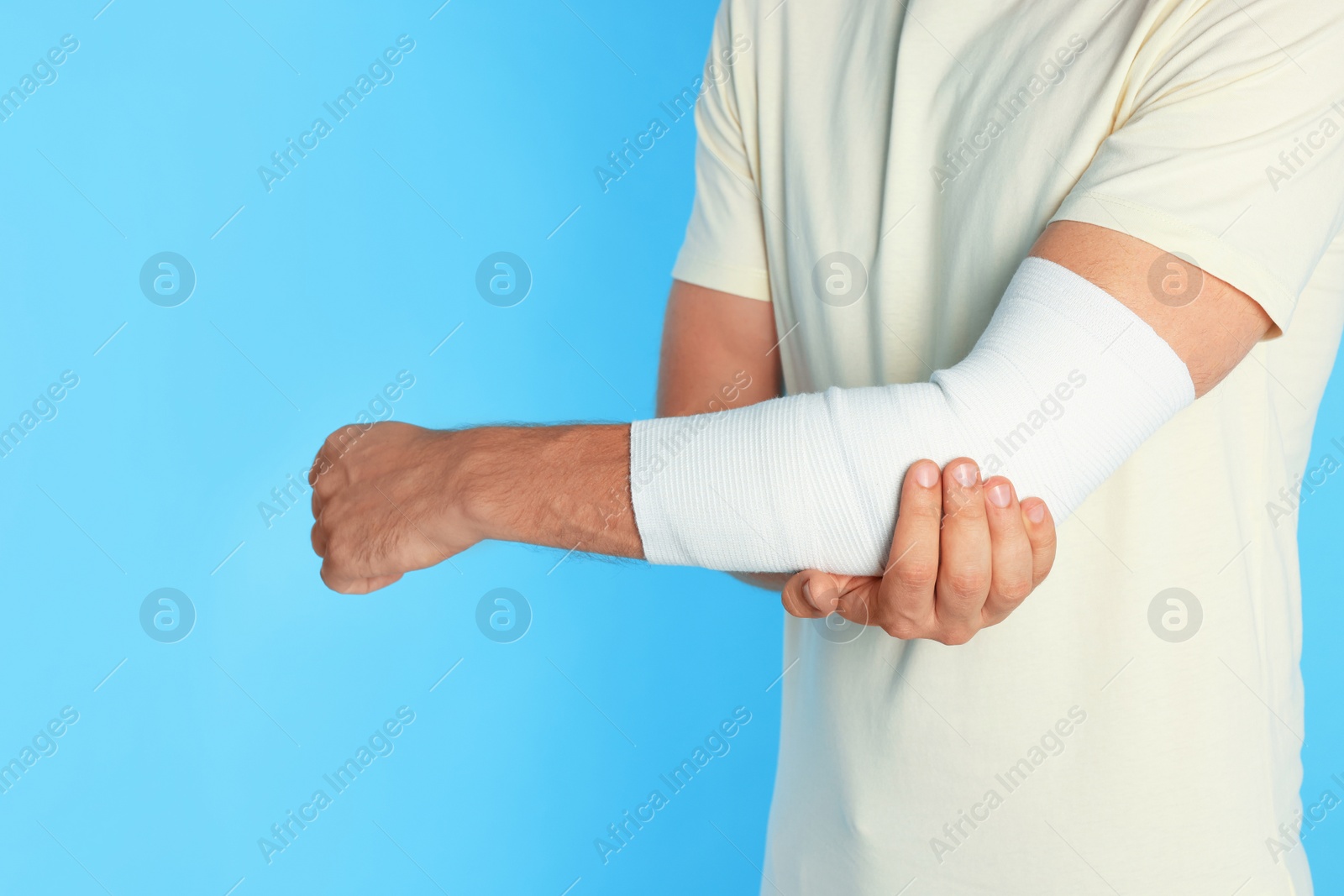 Photo of Man with arm wrapped in medical bandage on light blue background, closeup