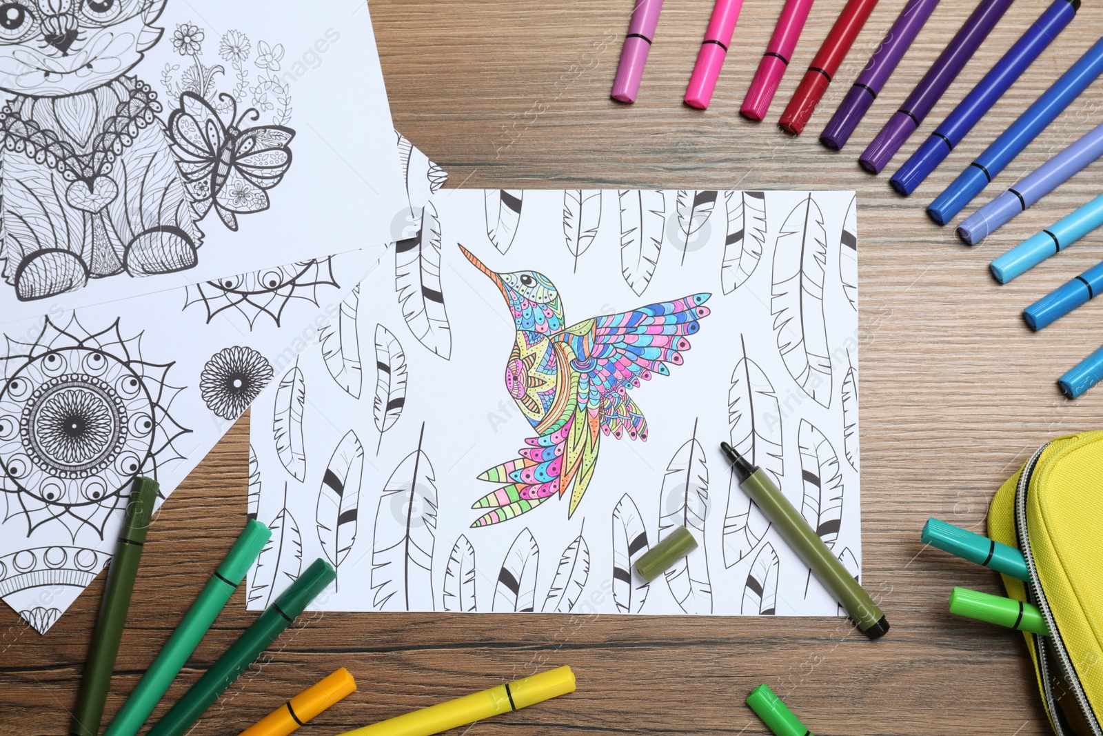 Photo of Antistress coloring pages and felt tip pens on wooden table, flat lay