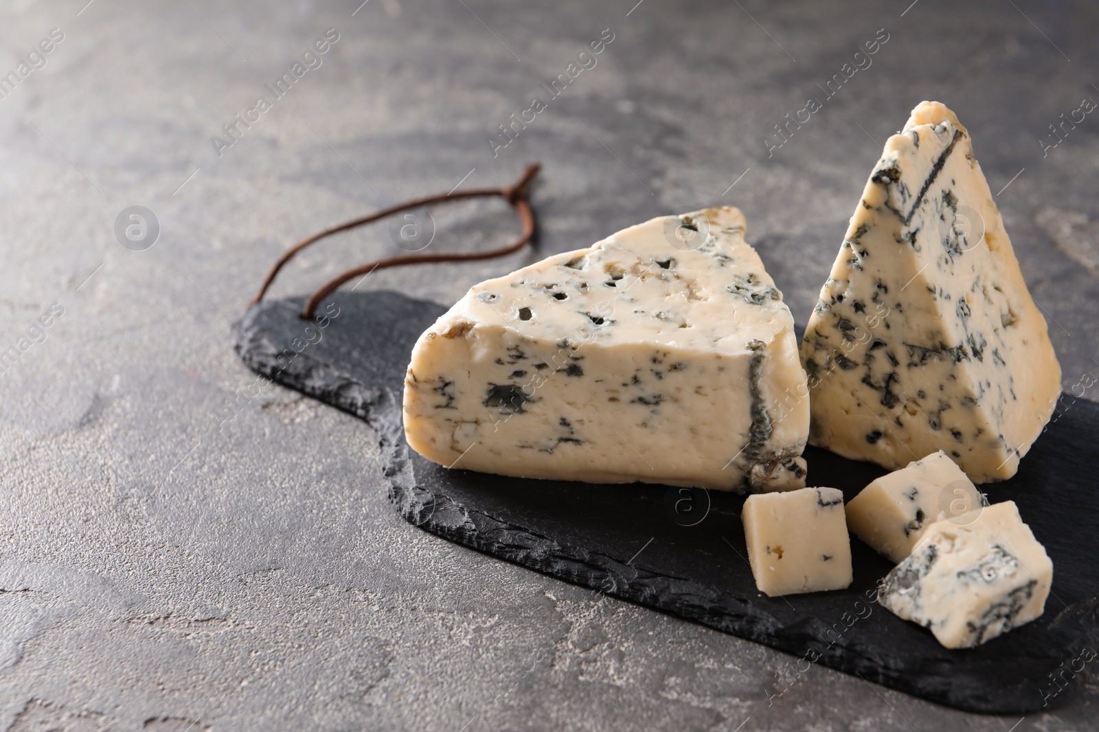 Photo of Slate board with delicious blue cheese on stone surface. Space for text