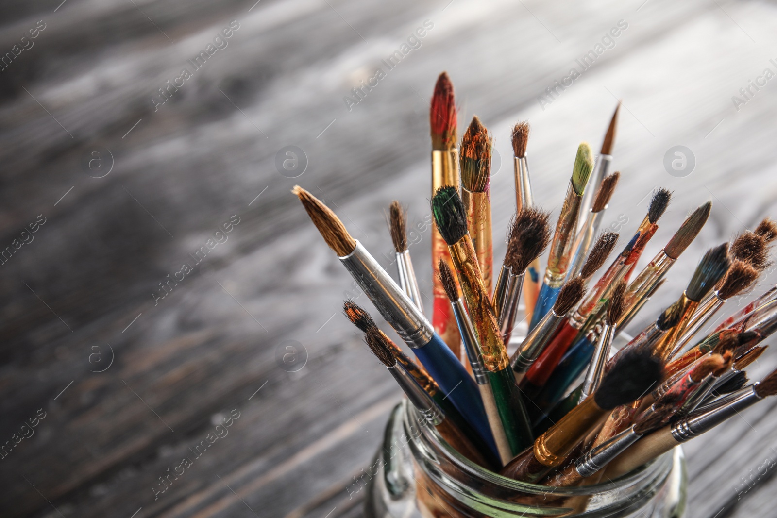 Photo of Jar with paint brushes on wooden table, closeup. Space for text