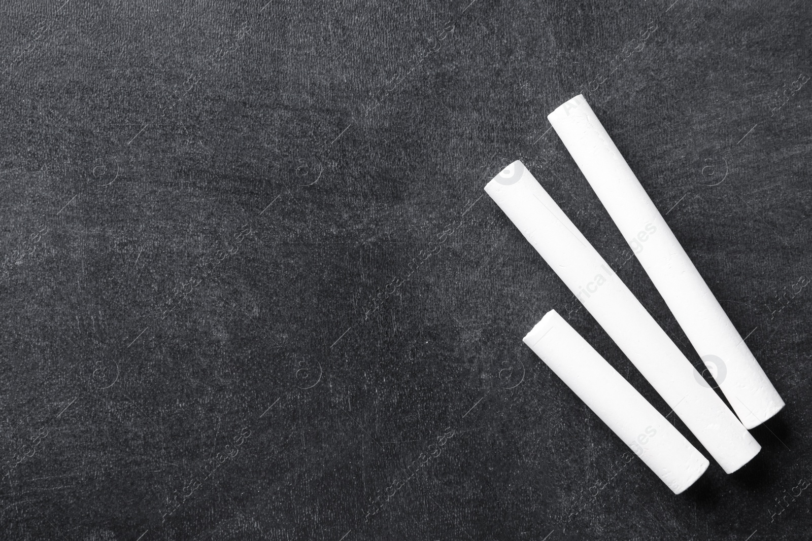 Photo of Pieces of white chalk on blackboard, flat lay. Space for text