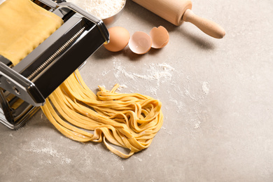 Pasta maker machine with dough and products on grey table, above view