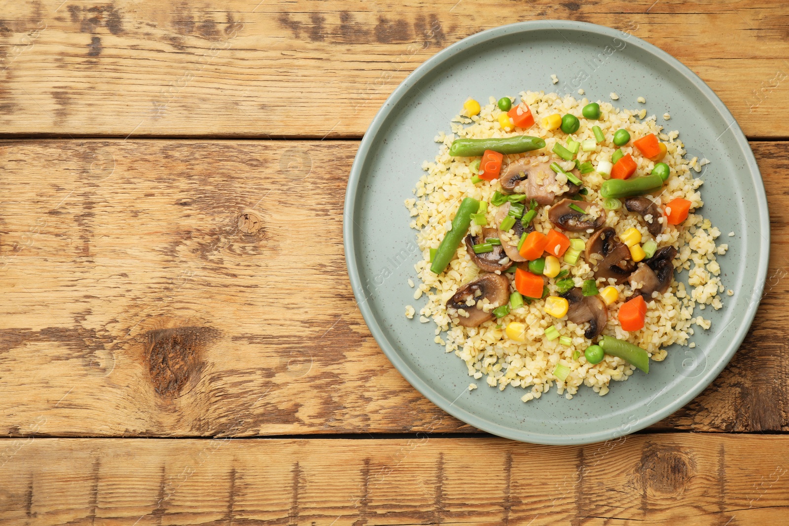 Photo of Delicious bulgur with vegetables and mushrooms on wooden table, top view. Space for text