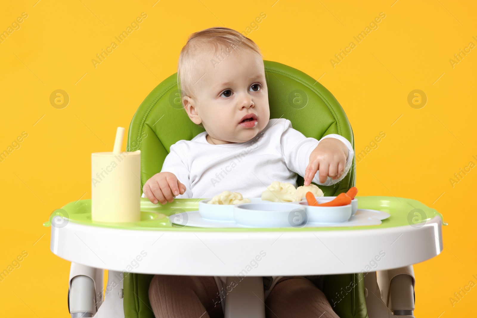 Photo of Cute little baby with healthy food in high chair on orange background