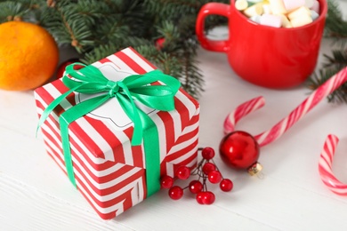 Photo of Christmas gift box, red berries and decorations on white table, closeup