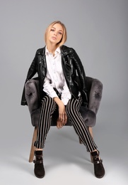 Young stylish woman with trendy shoes sitting in armchair on grey background