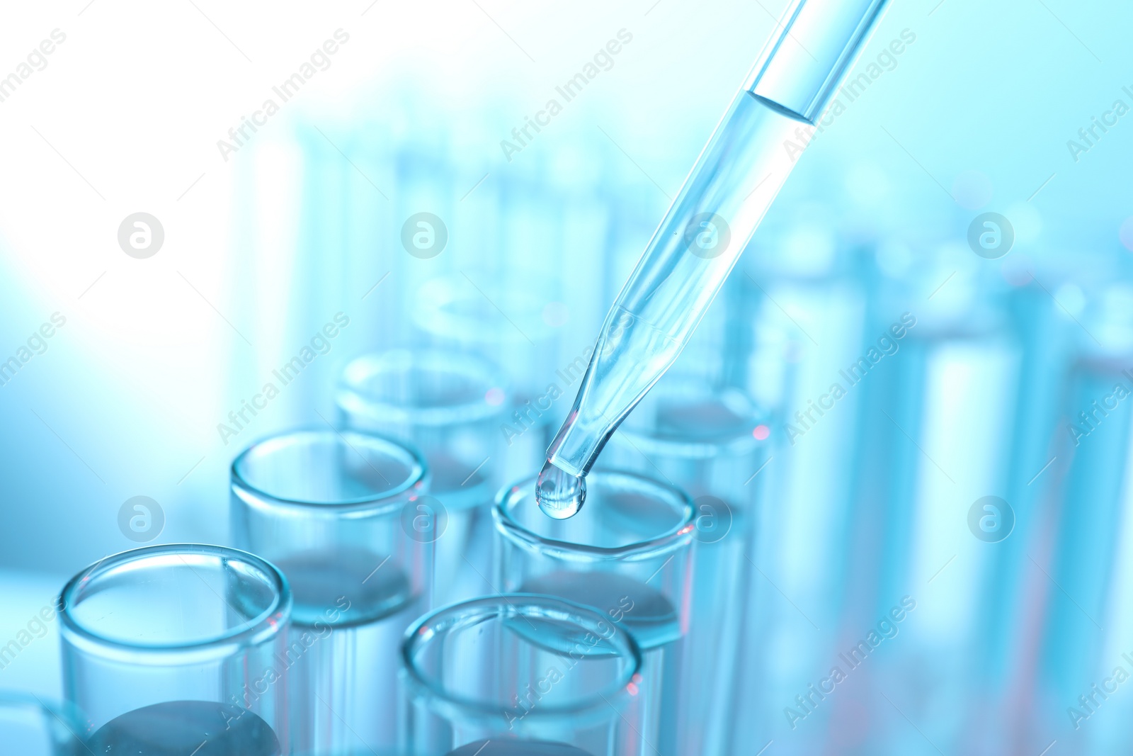 Photo of Dripping liquid from pipette into test tube on light blue background, closeup