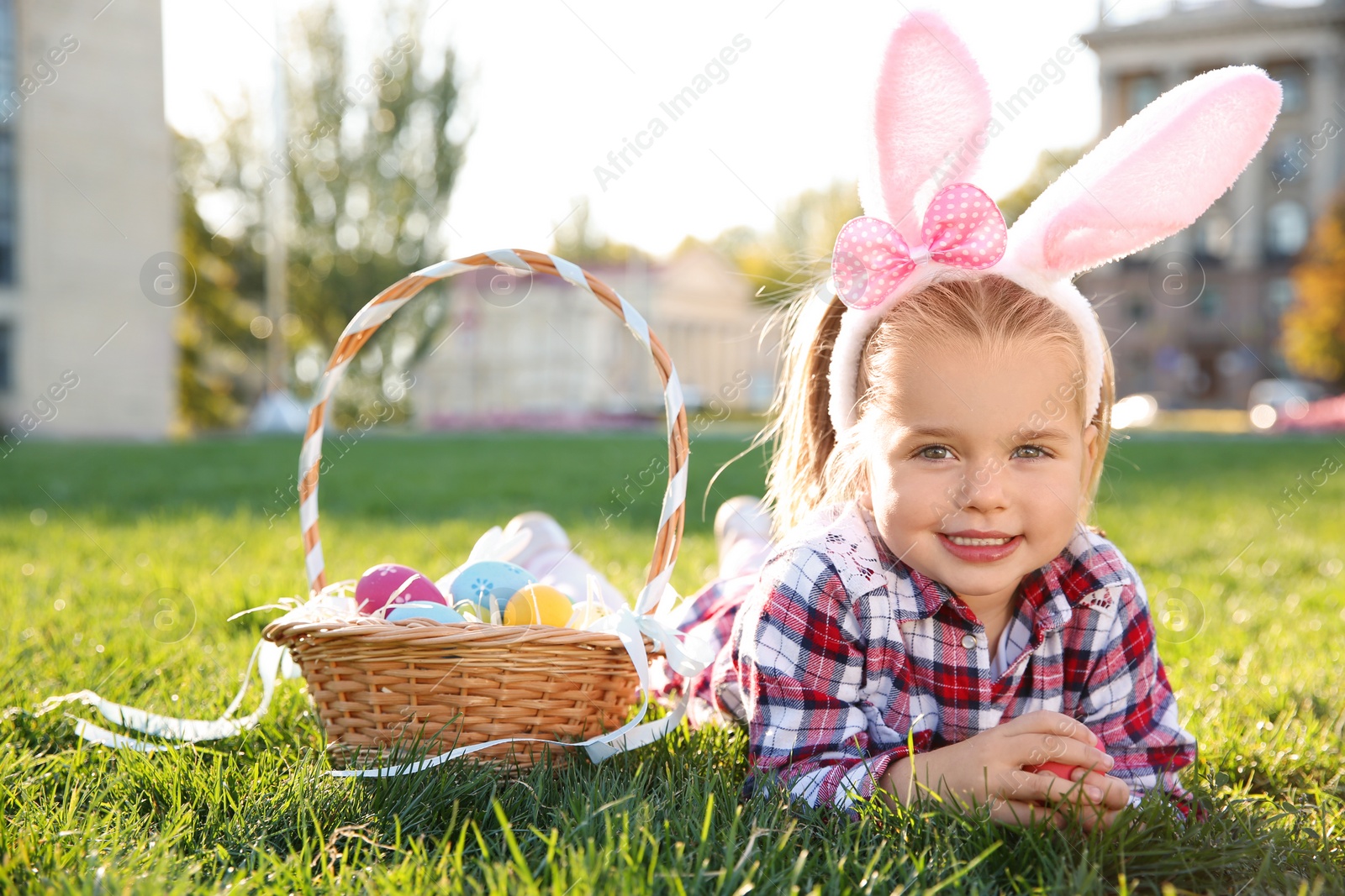 Photo of Cute little girl with bunny ears and basket of Easter eggs in park