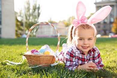 Cute little girl with bunny ears and basket of Easter eggs in park