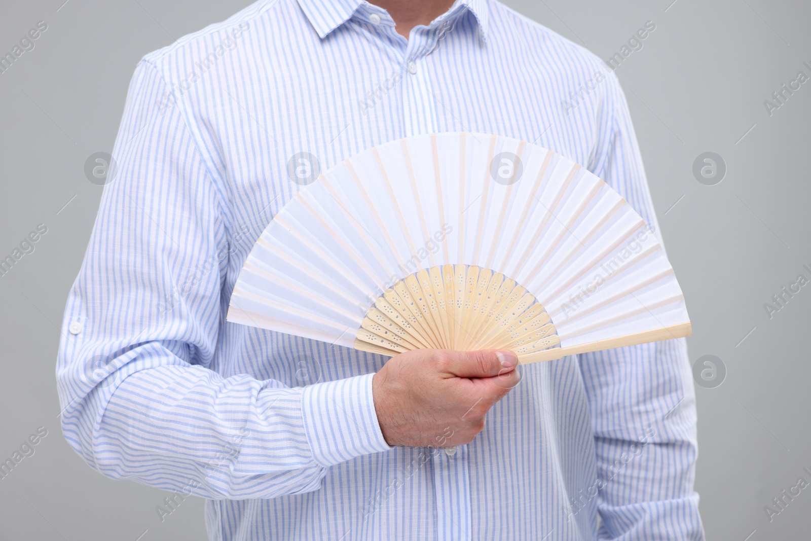 Photo of Man holding hand fan on light grey background, closeup